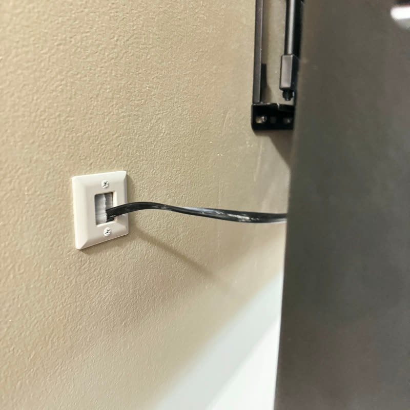 TV cable running into a wall plate behind a mounted TV